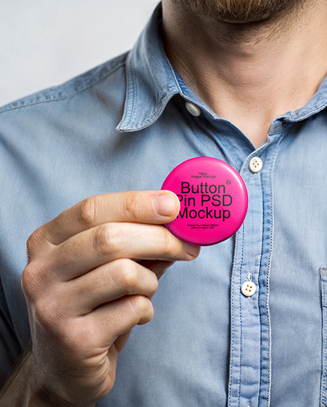 A Man Wearing a Denim Shirt Holds a Pin-Back Button Mockup