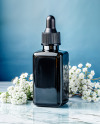 Dark Amber Oil Tincture Square Bottle on a Marble Surface with Flowers Mockup