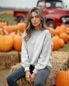 Young Woman in Sweatshirt Sitting on Hay Block with Pumpkins Around
